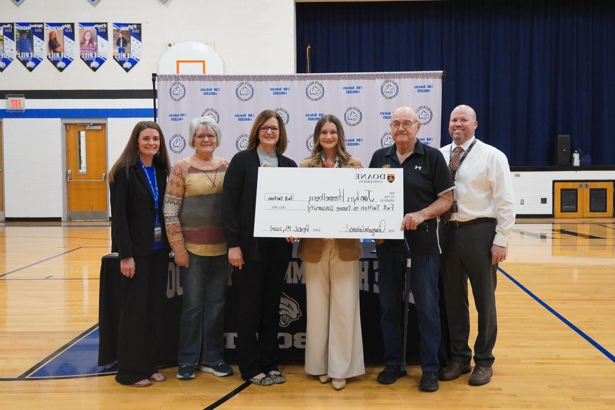 Six people stand in front of a white backdrop inside a school gymnasium. They're holding a giant check that reads "Pay to the order of Jaelyn Himmelberg; Full tuition to 澳门威尼斯人网址; Congratulations!"